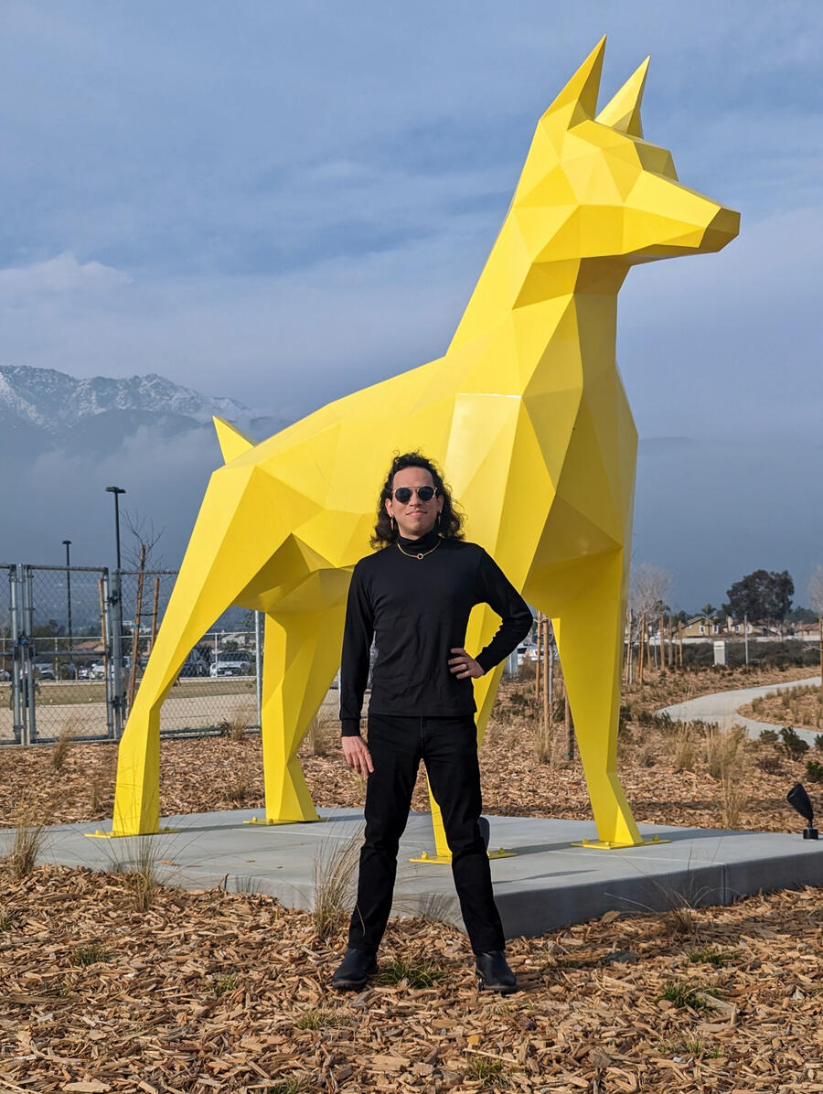 A photo of me standing in front of a large yellow polyhedral dog statue in 2024.